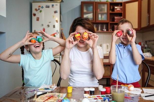 Mamá y niños juegan con huevos de Pascua pintados como ojos en casa en la cocina