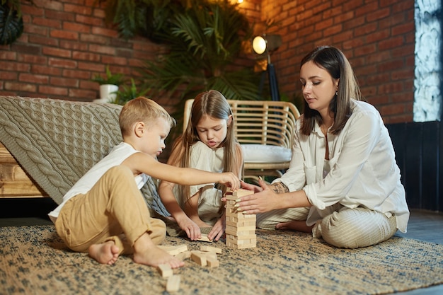 Mamá y niños juegan squirl tower. La mujer, la niña y el niño juegan un juego de rompecabezas familiar. Día libre familiar