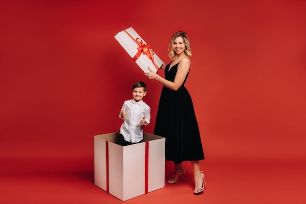 Mama öffnet ein riesiges Weihnachtsgeschenk, in dem ein Junge steht und die Klasse auf rotem Grund zeigt