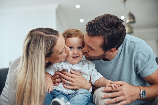 Mamá, papá y bebé se besan en el sofá en la sala de estar de la casa de familia feliz, padres jóvenes e hijos juntos Aman la felicidad y la pareja besa a los niños con una sonrisa mientras se sientan en el sofá en el apartamento de Nueva York