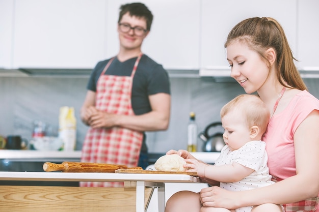 Mamá, papá y bebé cocinando pasteles juntos en la cocina y sonriendo en casa