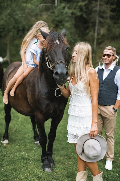 Mamá y papá caminando con sus dos hijas lindas montando a caballo en la naturaleza