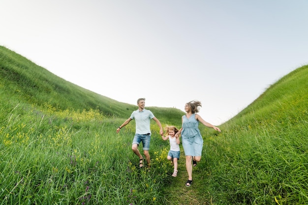 Mamá papá e hija caminan en la hierba verde Feliz familia joven pasando tiempo juntos corriendo al aire libre El concepto de vacaciones familiares