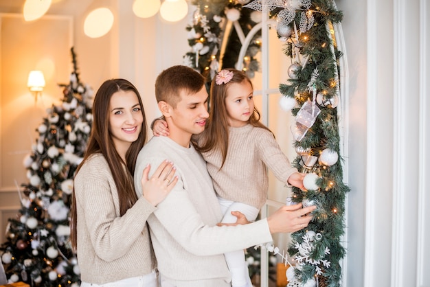 Mamá, papá e hija decoran la casa para Navidad. Retrato de una familia en un fondo de año nuevo