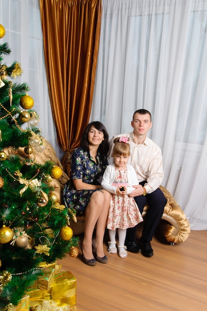 Mamá, papá e hija posando con el árbol de navidad