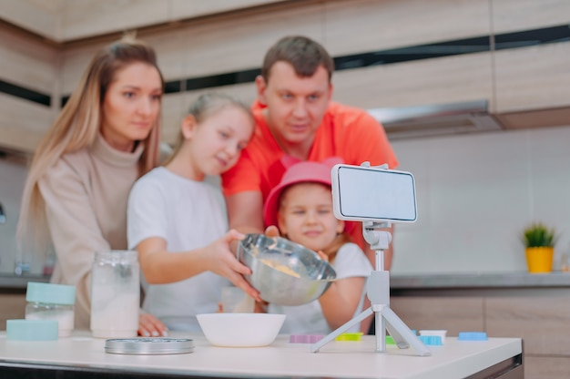 Mamá con papá les enseña a dos hijas a cocinar masa en la cocina.