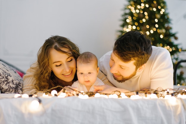 Mamá y papá felices se acuestan en la cama junto a su bebé