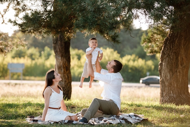 Mama, Papa hebt sein Baby hoch in die Luft und sieht sie lächelnd an. Glückliche Eltern verbringen Zeit damit, mit Sohn im Park am Sommertag zu spielen. selektiver Fokus.