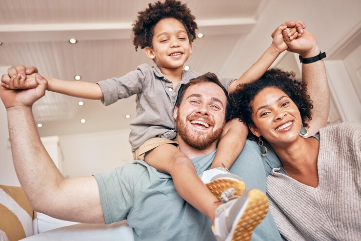 Foto mamá papá y niño sobre los hombros a cuestas y retrato en casa con una sonrisa tomados de la mano y solidaridad casa de familia interracial madre y padre con hijo jugando juegos de avión y vinculándose con amor
