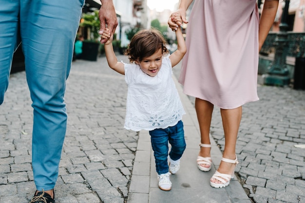 La mamá papá sostiene a la niña Joven familia feliz padre hija madre caminando por las calles cerca de la arquitectura antigua del casco antiguo al aire libre El concepto de vacaciones familiares y viajes