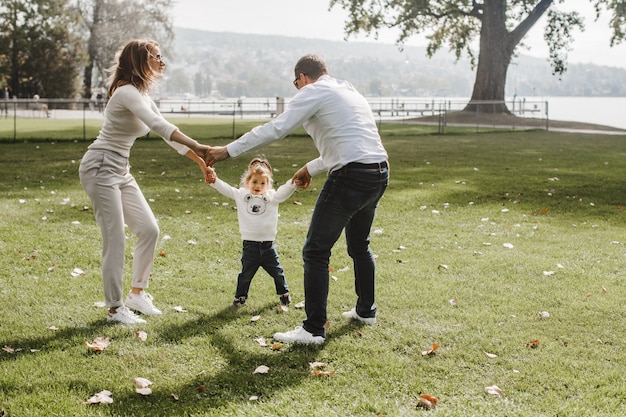 Mama, Papa und Tochter tanzen im Park in der Nähe des Sees
