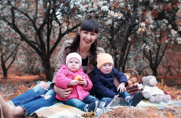 Mamá del parque de otoño con gemelos en plaid al aire libre en el jardín de manzanas