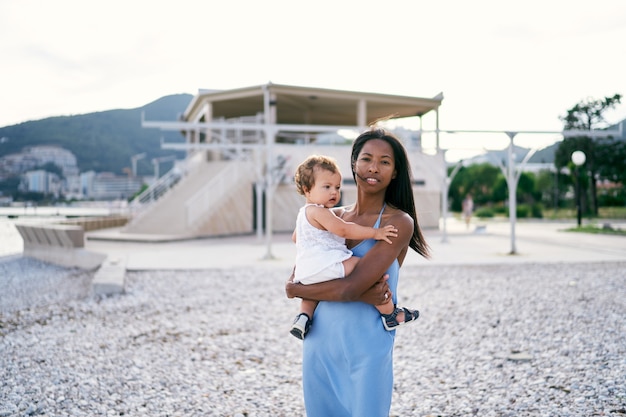 Mamá con una pequeña hija en brazos se encuentra en la playa junto al mar