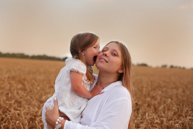 Mamá con una pequeña hija rubia están de pie en un campo de trigo, la ternura de la familia