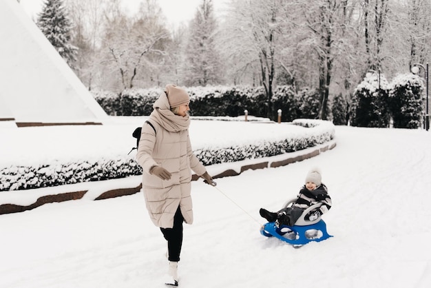 Mama reitet einen süßen Jungen in einem Schlitten in der schneeaktiven Lifestyle-Winterfamilie