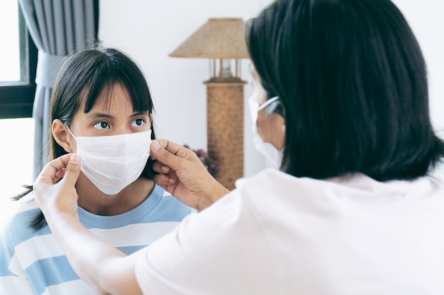 Mamá revisando a su hija Temperatura. Están debajo de una mascarilla quirúrgica que cubre la boca y la nariz.