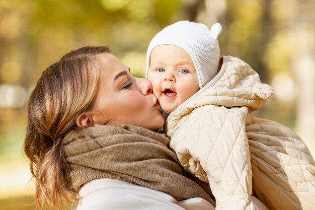 Mamá riendo con su bebé en un parque de otoño en un día soleado. De cerca. Amor y ternura.