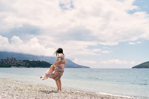 Mamá rodea a una niña en una playa de guijarros