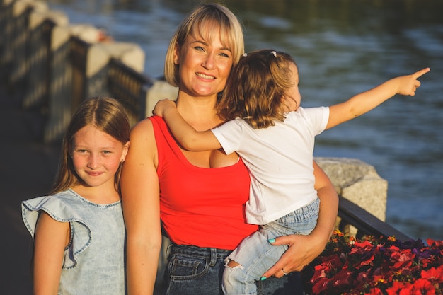 Mamá rubia hermosa en una camiseta roja con sus hijas en el terraplén. retrato de grupo