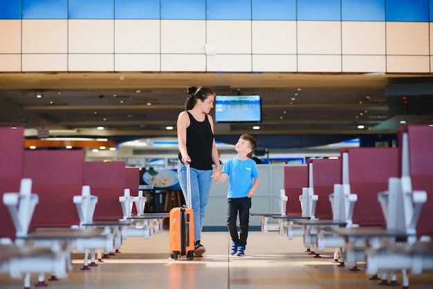 Mamá saludando a su hijo en el aeropuerto con una maleta