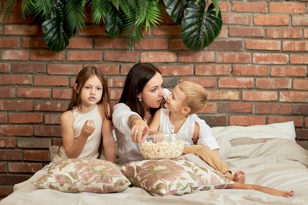 Mamá se sienta en la cama con su hijo y su hija y mira una película.