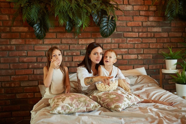 Mamá se sienta en la cama con su hijo y su hija y mira la película