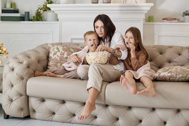 Mama sitzt mit ihrem Sohn und ihrer Tochter auf der Couch und schaut sich einen Film an. Eine Frau, ein Junge und ein Mädchen essen Popcorn, während sie einen Film schauen. Die Familie ruht sich am Wochenende zu Hause aus