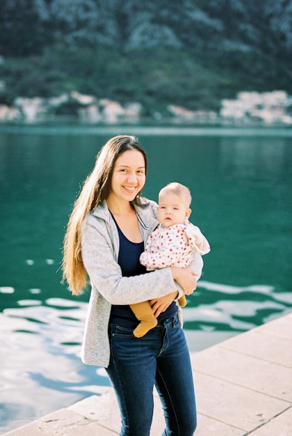 Mamá sonriente con un bebé en brazos se encuentra en el muelle