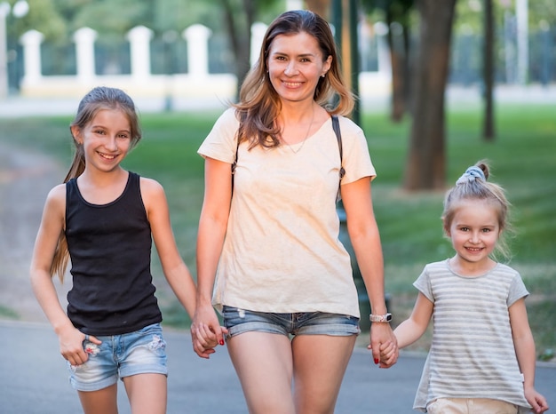 Mamá sonriente con hijas pequeñas caminando tomándose de la mano