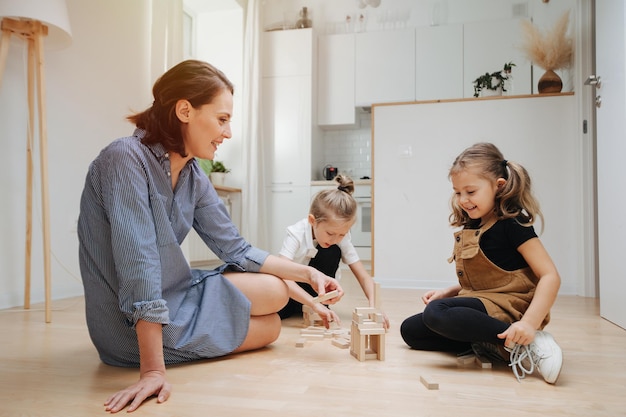 Mamá sonriente jugando con sus hijos en el piso Construyendo con bloques de madera