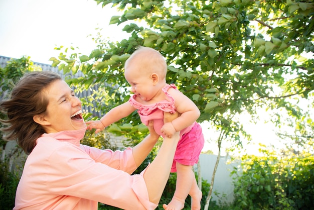 Mamá sonriente y pequeña hija rubia se divierten al aire libre en el jardín al aire libre familia feliz