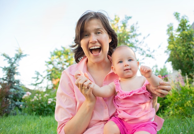 Mamá sonriente y pequeña hija rubia se divierten al aire libre en el jardín al aire libre familia feliz