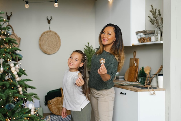 Mamá sonriente y su hija sostienen galletas navideñas en su cocina