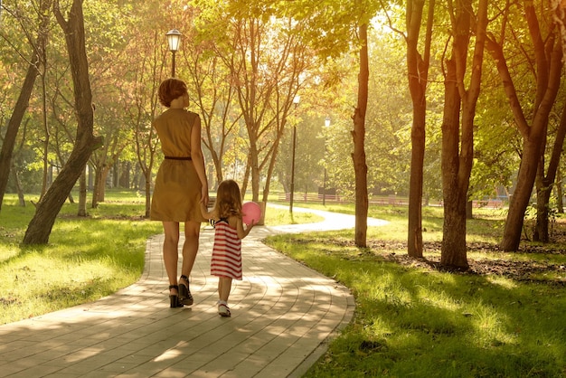 Mamá sostiene la mano de una niña con un globo en el parque Primer apretón de manos Familia feliz mamá hija