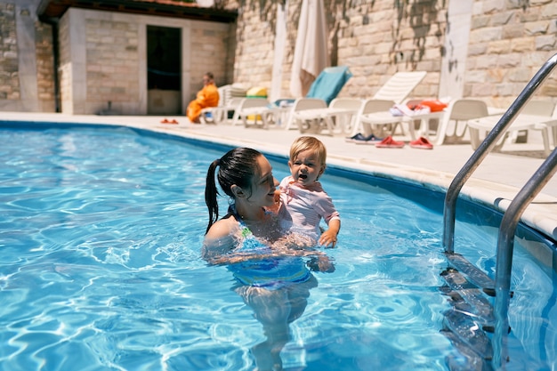 Mamá sostiene a una niña llorona en sus brazos en la piscina