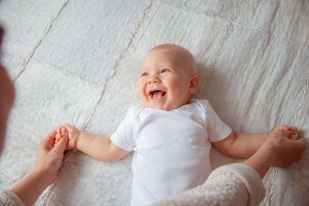 Mama spielt mit dem Baby, gibt ihm eine Massage und kontrolliert seinen Körper, Kind in einem weißen Body