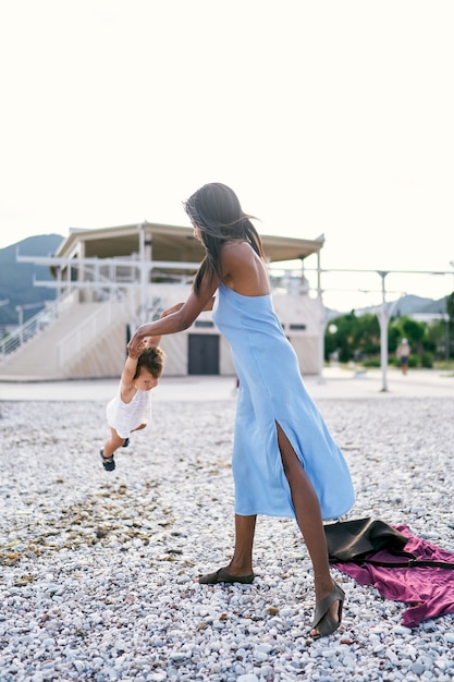 Mama steht am Strand und schwingt kleines Mädchen an den Armen