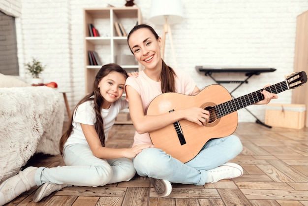 Mamá y su hija están sentadas en el suelo con la guitarra.