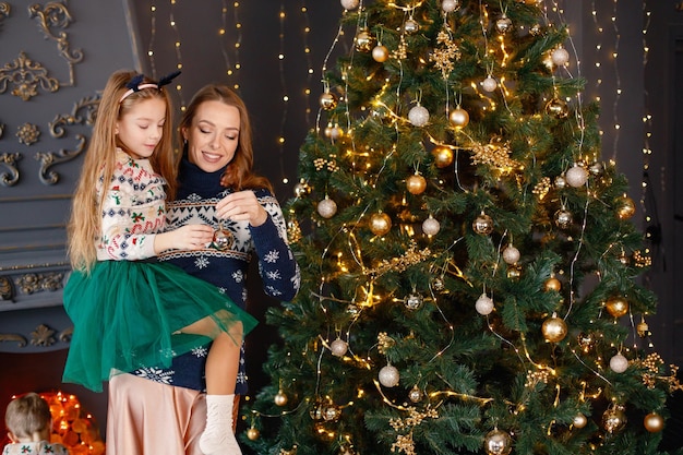 Mamá y su hija paradas cerca del árbol de Navidad y abrazándose