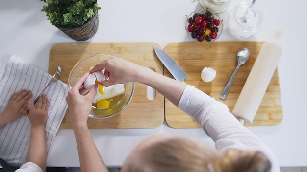 Mamá con su hija pone huevos crudos en la masa para tortitas de requesón