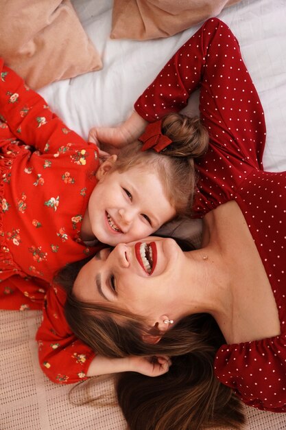 Mamá y su pequeña hija se acuestan en la cama uno frente al otro son felices