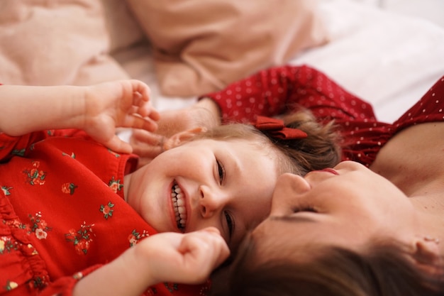 Mamá y su pequeña hija se acuestan en la cama uno frente al otro son felices