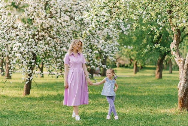 Mamá y su pequeña hija caminan por un floreciente jardín de primavera