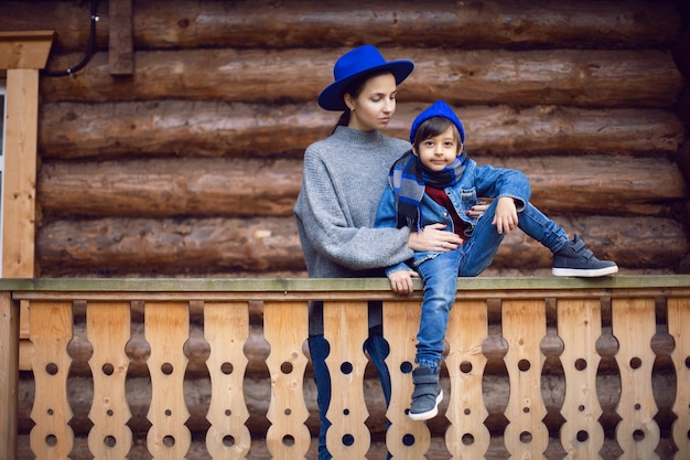 Mamá con un suéter y un sombrero azul con un niño sentado en el porche