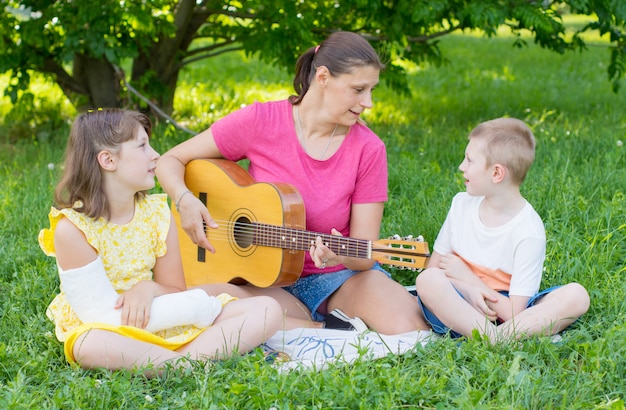 Mamá con sus dos hijos tocan la guitarra en el parque.