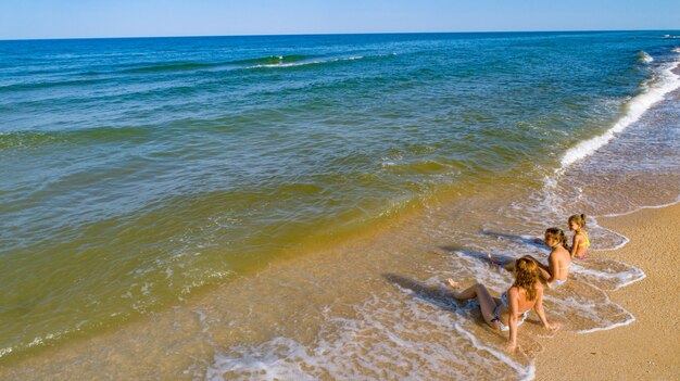 Mamá y sus hijas disfrutando de la vista al mar mientras están sentadas en la orilla del mar en las olas