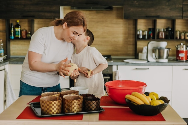 Mamá con sus hijos pequeños en la mesa de la cocina en casa preparando juntos la masa para hornear un pastel de vacaciones