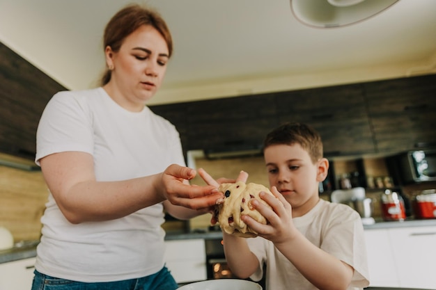 Mamá con sus hijos pequeños en la mesa de la cocina en casa preparando juntos la masa para hornear un pastel de vacaciones