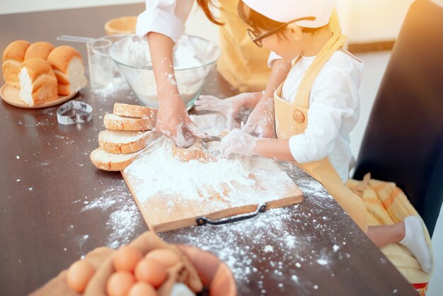 Mamá tailandesa enseñando a niños asiáticos para cocinar alimentos. Preparando un ingrediente con harina y pan.