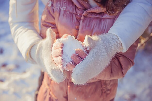 Mamá tiene las manos de sus hijas en sus guantes de piel en la calle en la nieve del invierno